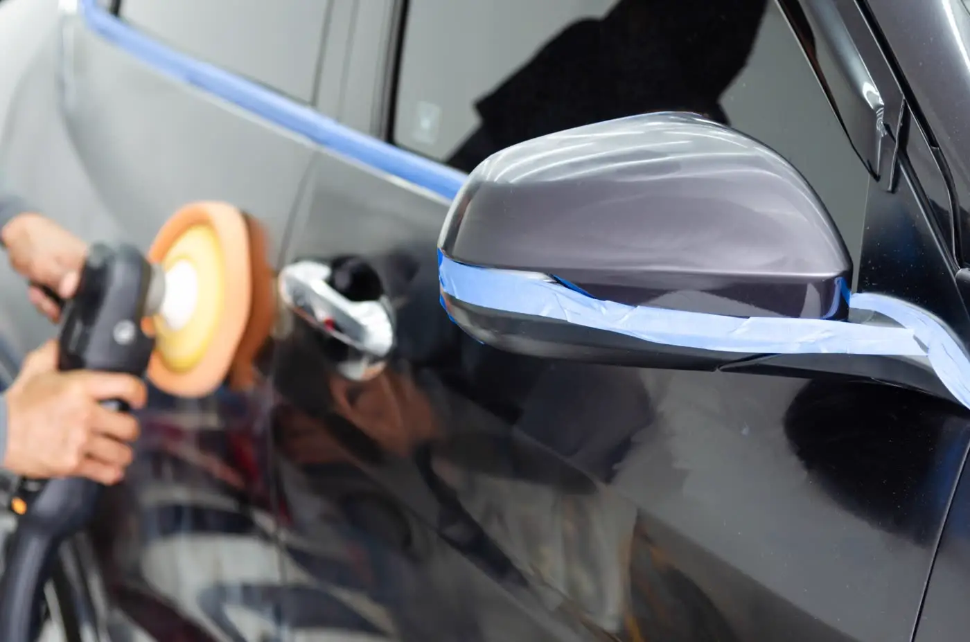 Masking tape being applied around a wing mirror before machine polishing