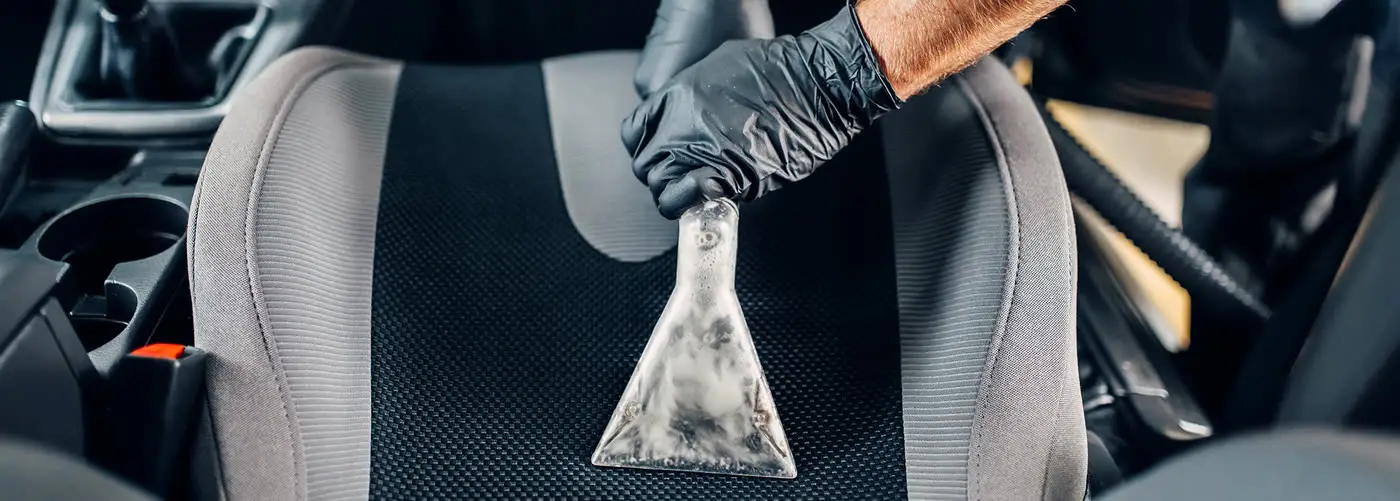 Detailer extracting a car seat with a steam cleaner